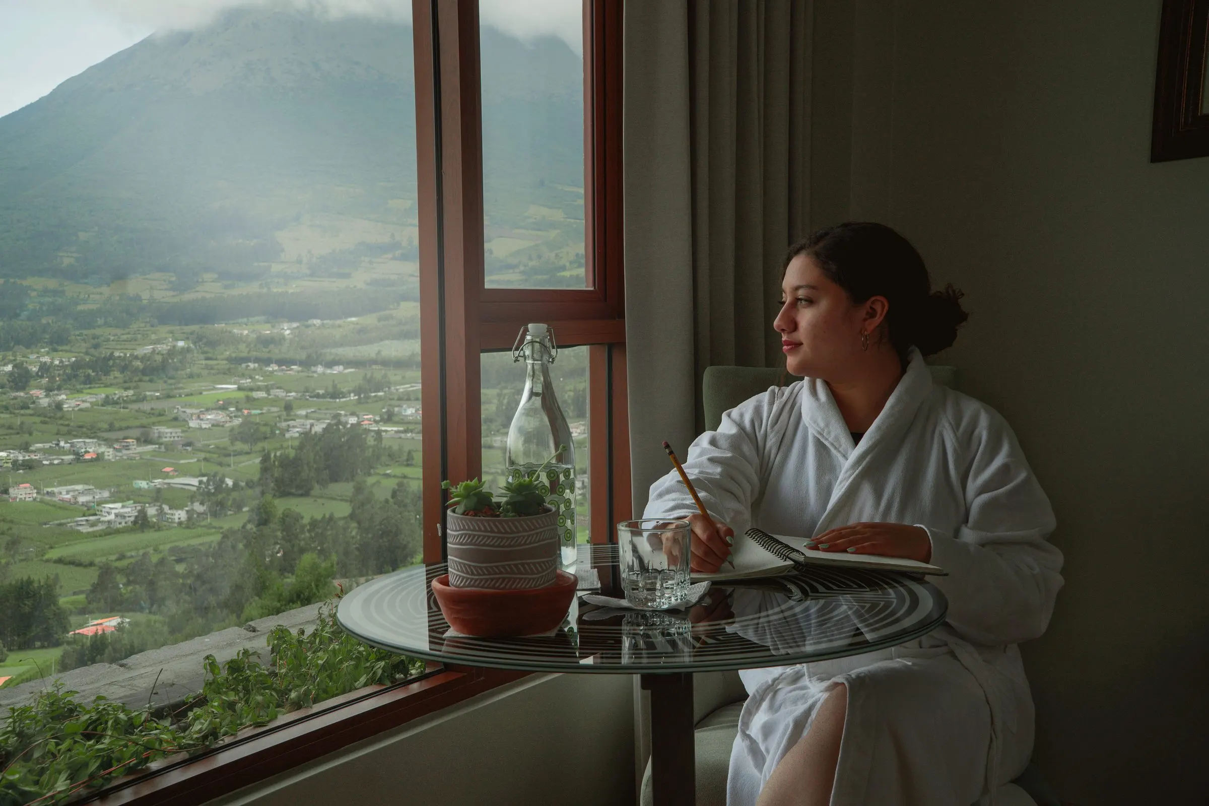 Gast im Bademantel liest am großen Fenster, im Hintergrund Tal und Berge