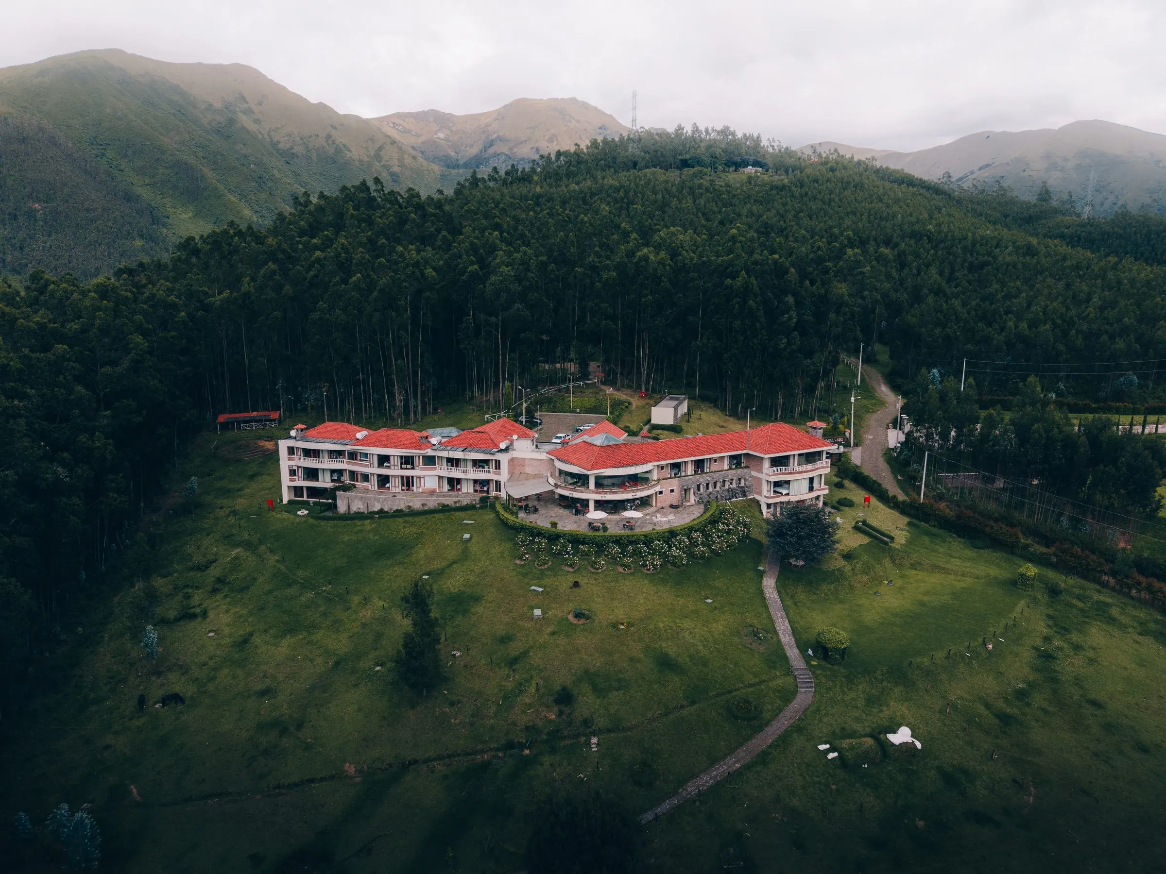 Luftaufnahme des Hotels am Hang, umgeben von Wald und Bergen