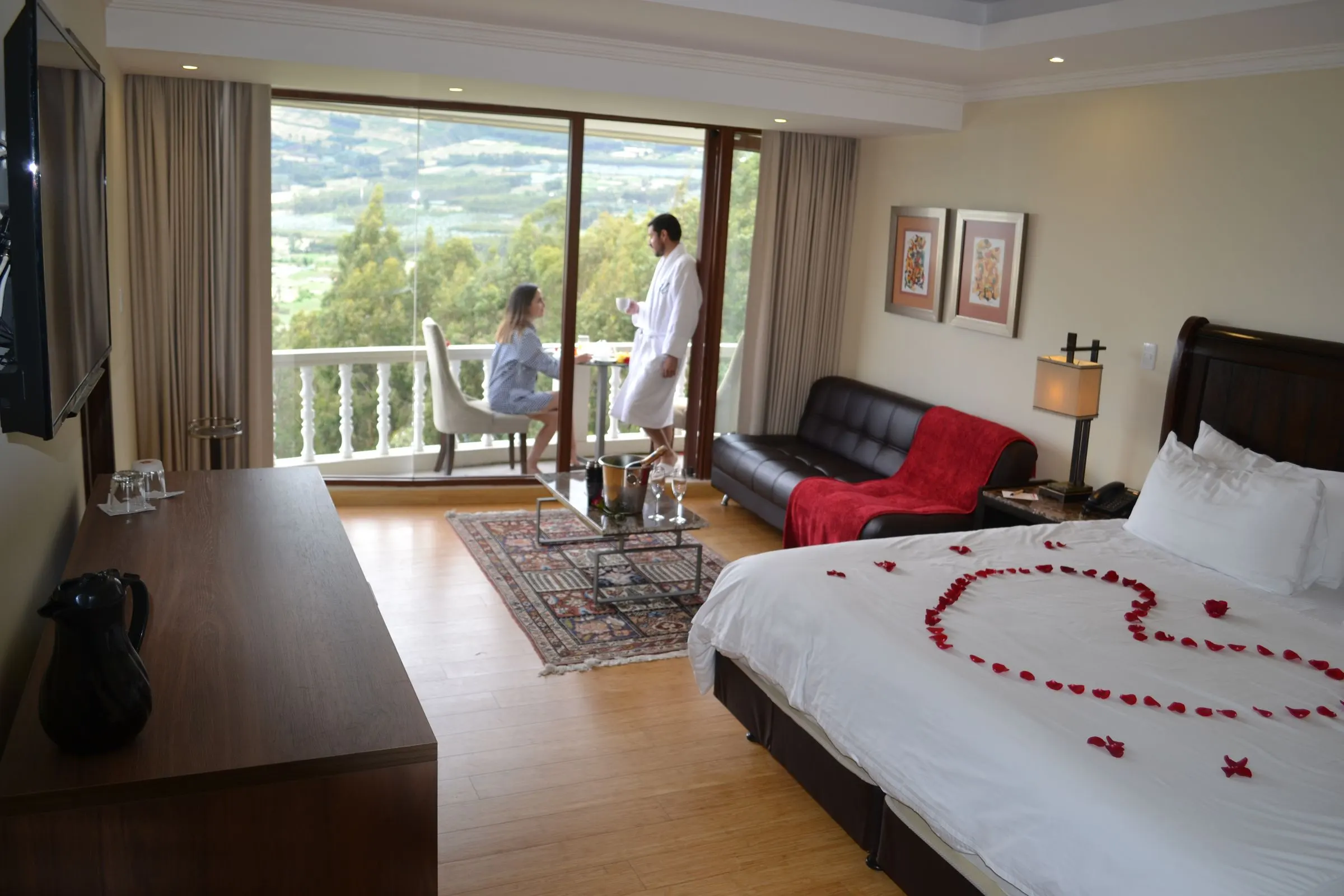 Cama de la suite decorada con pétalos de rosa y el balcón al fondo